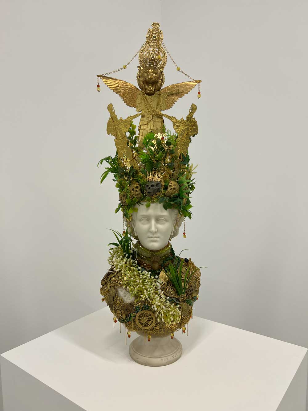 Mixed-media sculpture: white marble female bust adorned with golden wings, green foliage, skulls and Baroque ornaments on a plinth — contemporary art advisory