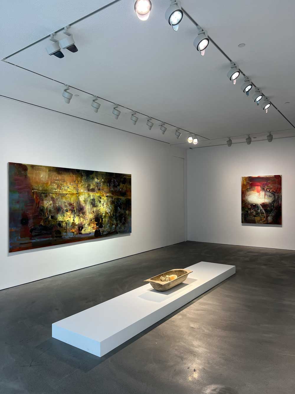 Gallery interior with two large gestural dark paintings in ochre, crimson and black tones, and a ceramic vessel on a low plinth — art advisory acquisition context