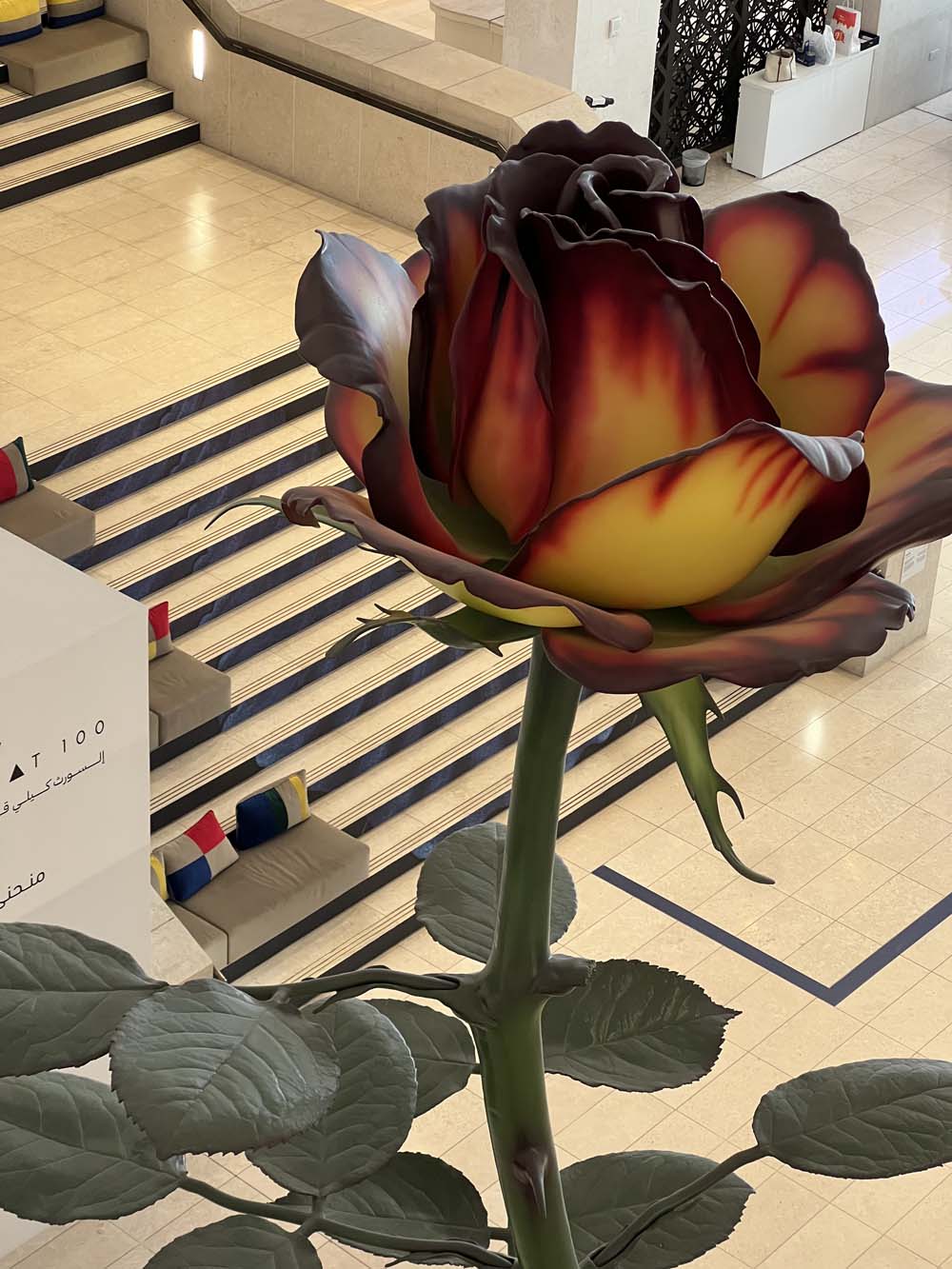 Oversized resin rose sculpture in vivid red and yellow in a museum gallery in Doha — contemporary art advisory in the Middle East