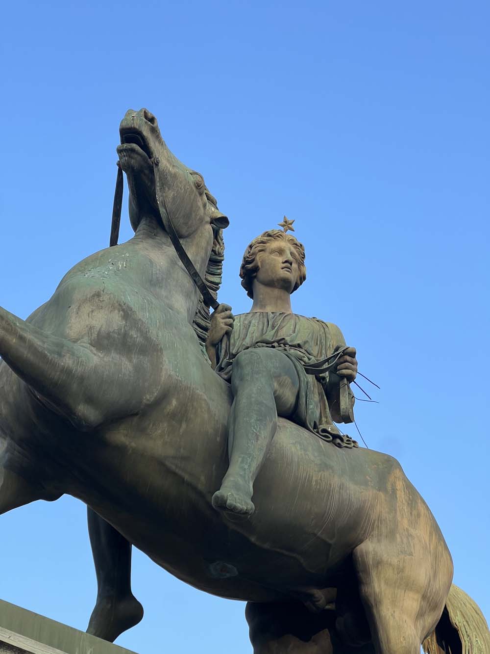 Bronze equestrian sculpture with a female figure wearing a star crown on a rearing horse against a blue sky, Piazza Castello Turin