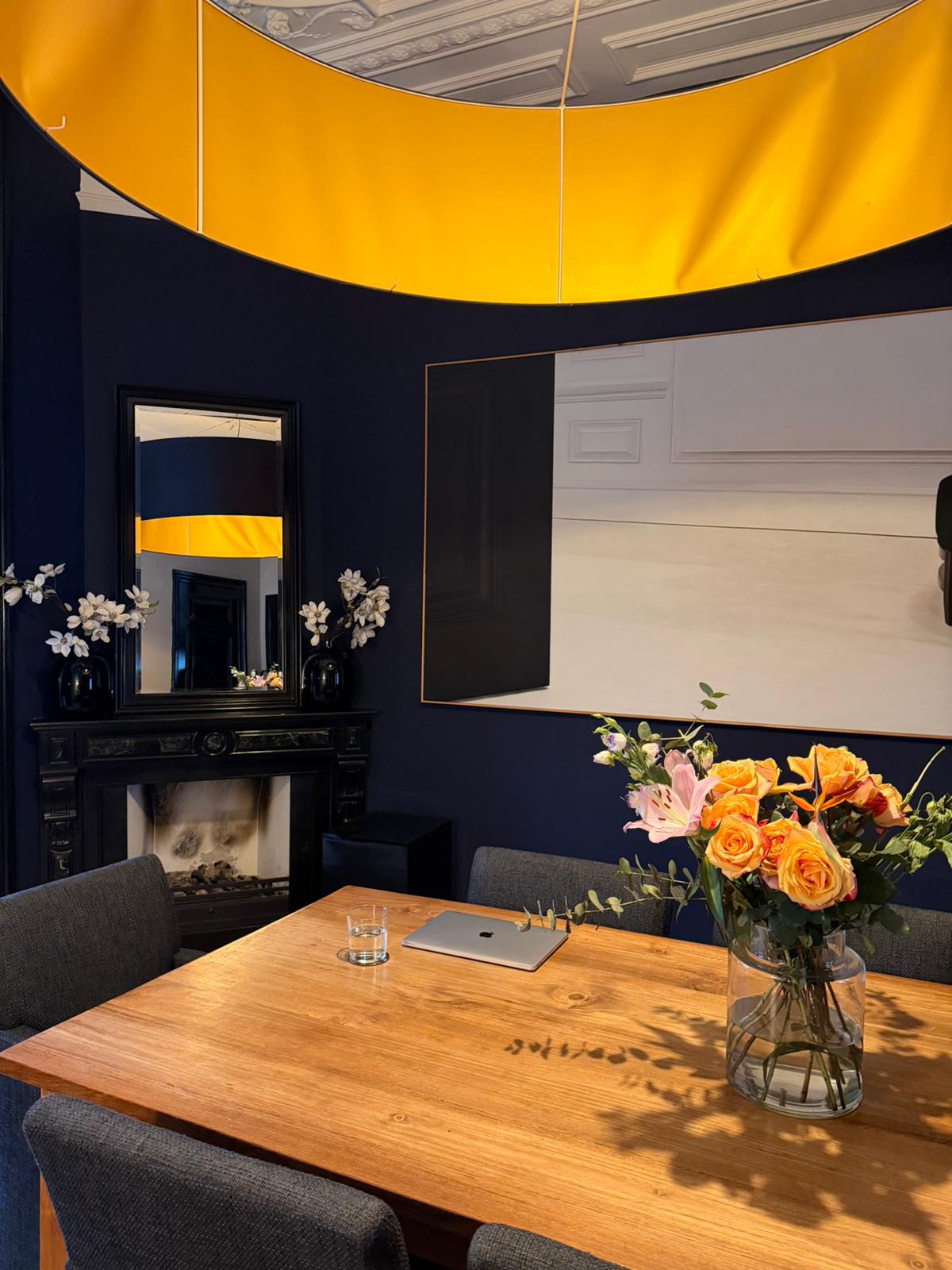 AN Art Advisory studio in The Hague: consultation room with wooden table, fresh flowers, contemporary painting and a circular gold pendant lamp