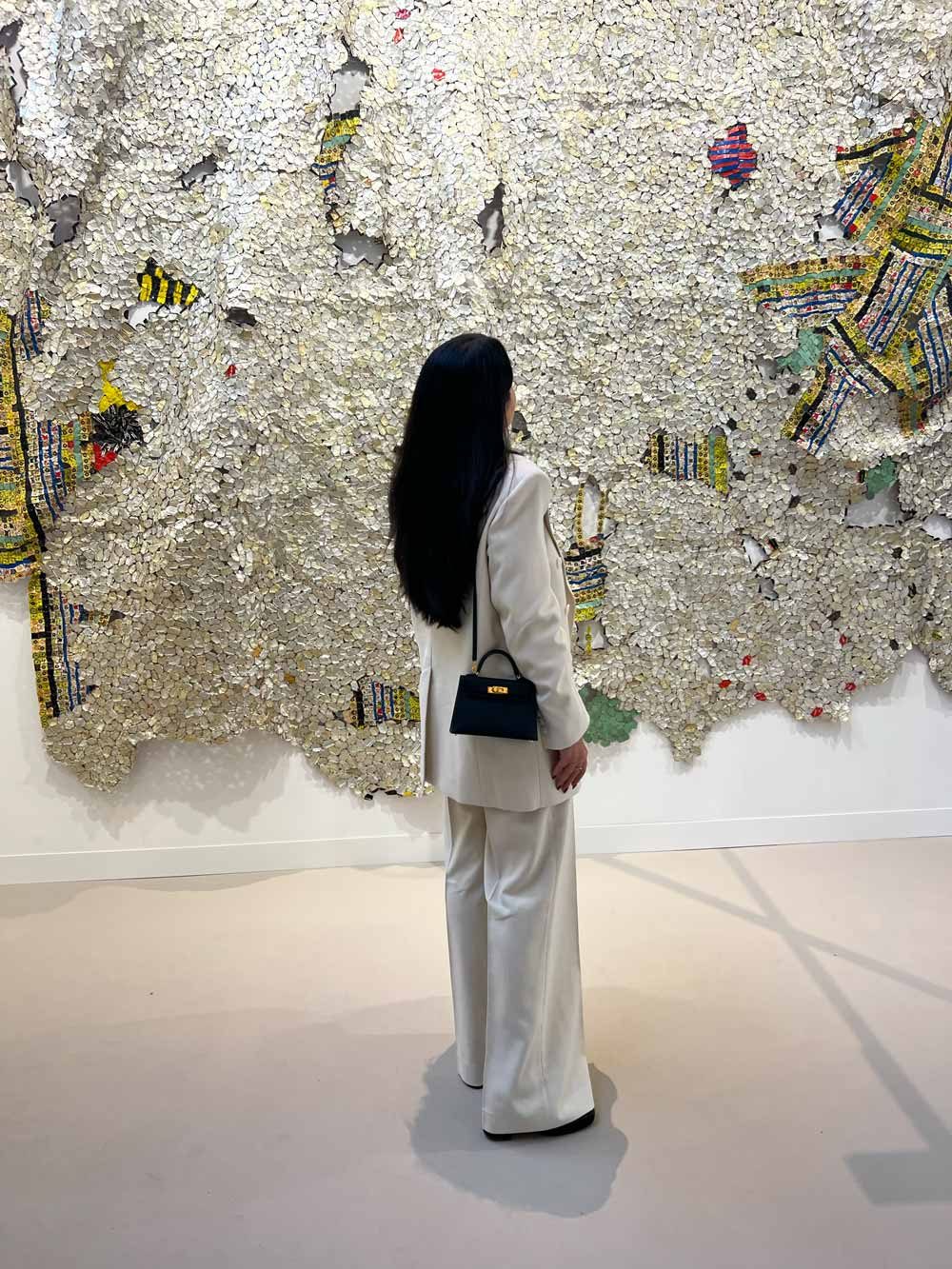 Collector in a white suit contemplating a large mixed-media textile installation in a gallery — art advisory and wealth advisory