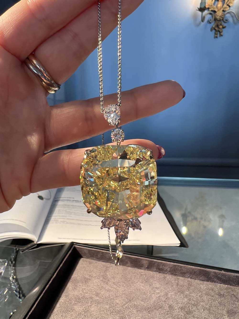 Large fancy yellow cushion-cut natural diamond pendant on a platinum chain with white diamond drops, held in hand — diamond advisory