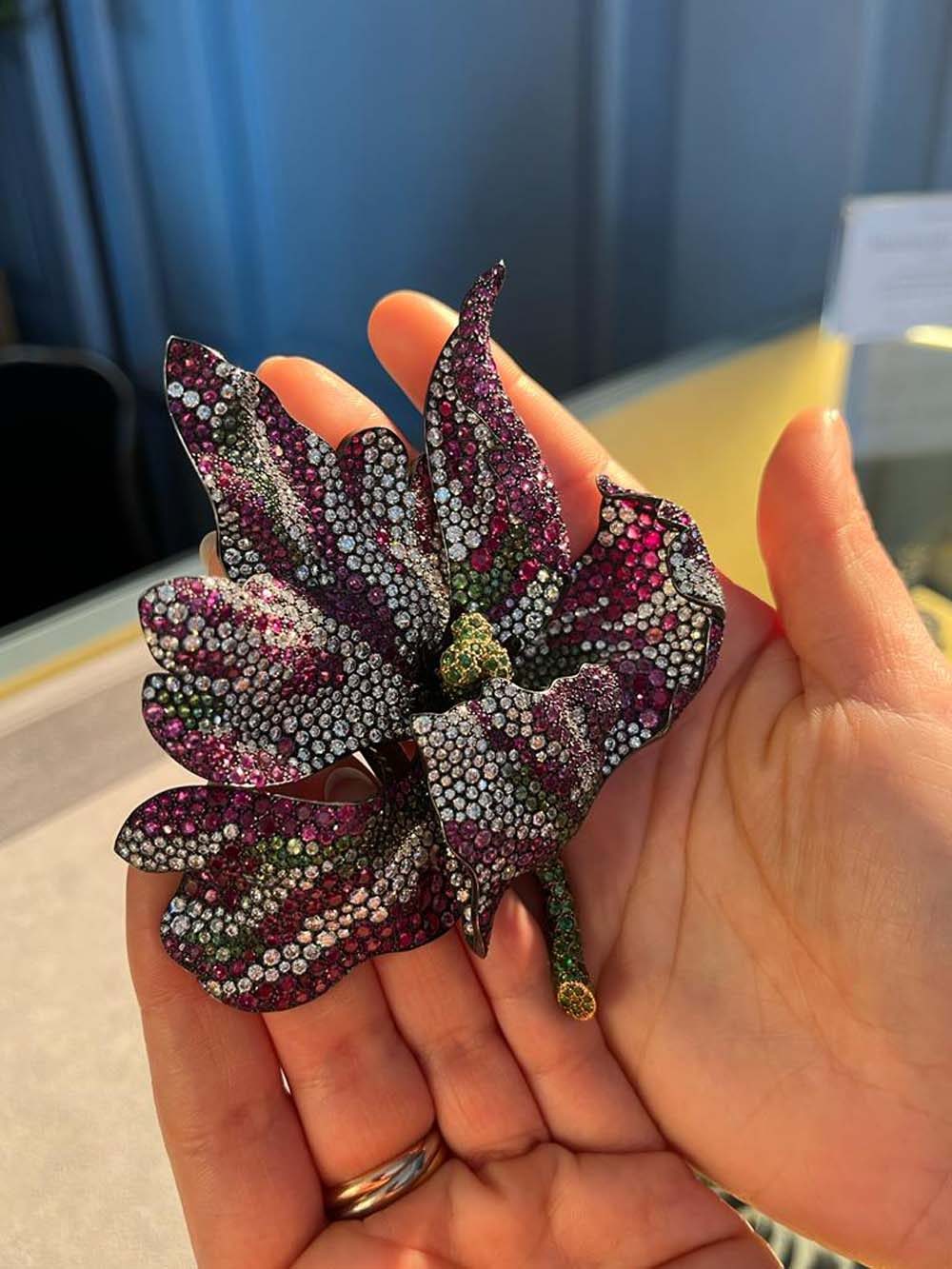 High jewelry flower brooch pavé-set with rubies, diamonds and emeralds held in hand — fine jewelry collection advisory