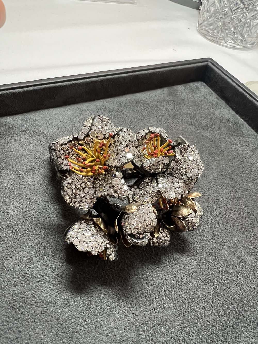 Antique diamond flower brooch with gold stamens in a velvet box alongside a black pearl bracelet watch — jewelry advisory and valuation
