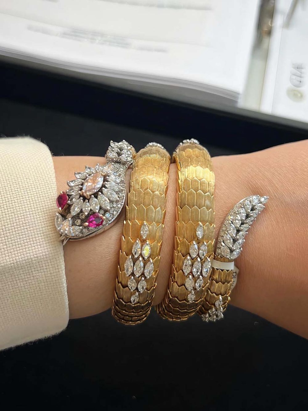 Stacked vintage gold Bulgari serpenti bracelets with diamond clasps and a ruby diamond brooch worn on wrist — fine jewelry collection management